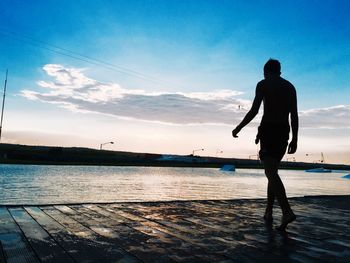 Shirtless man at riverbank against sky during sunset