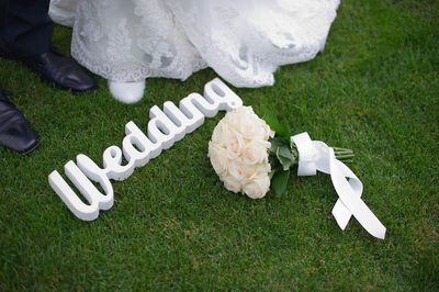 Low section of bride and groom standing by white rose and text on field