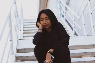 Young woman looking away while sitting on staircase