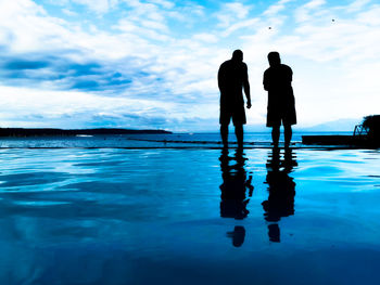Silhouette people standing by swimming pool against sky