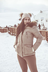 Portrait of beautiful young woman standing against sky in winter