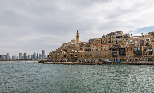 Buildings at waterfront against cloudy sky