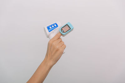 Cropped hand of woman holding thermometer against white background
