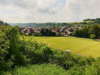 Scenic view of field by houses against sky