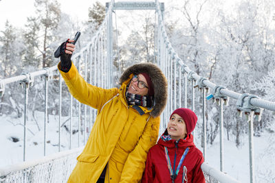 Mother and daughter taking a selfie on a bridge over a snowy river