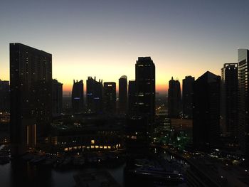 Illuminated buildings in city against clear sky at sunset