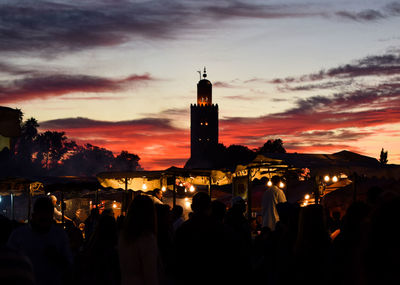 Silhouette people at illuminated building in city against sky during sunset