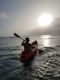 Rear view of man in sea against sky during sunset