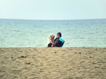 Friends on shore at beach against clear sky