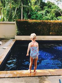 Rear view of woman standing by swimming pool against trees