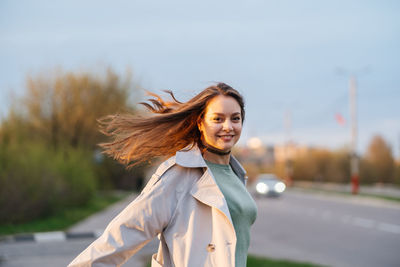 Beautiful smiling girl with long hair in a grey trench coat outdoors on the street spring