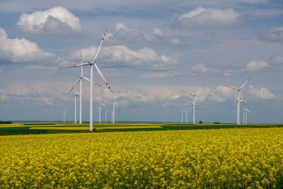 Wind turbines on landscape against cloudy sky