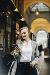 Young woman using phone while standing on laptop