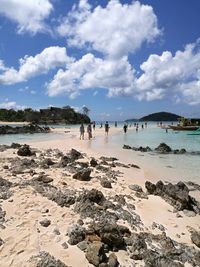 Distant view of people at beach against cloudy sky