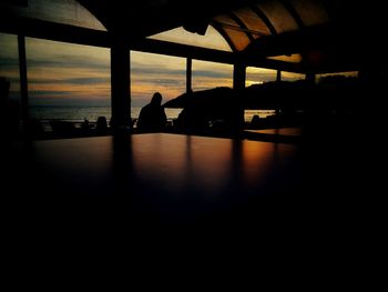 Silhouette people sitting by sea against sky seen through window