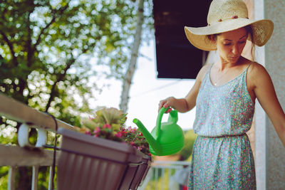 Woman watering plants with can while standing in balcony