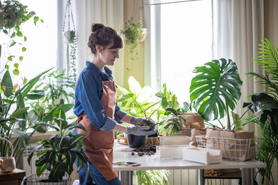 Side view of woman holding potted plant at home