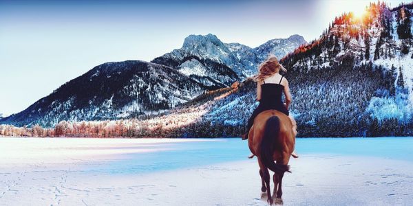 Woman riding horse at beach against mountains