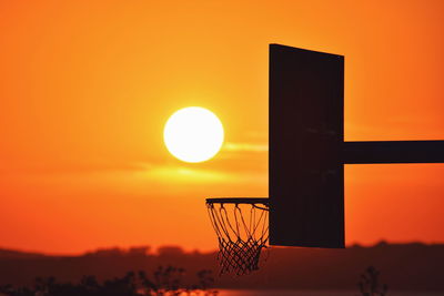 Silhouette basketball hoop against orange sky during sunset