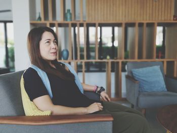 Mid adult woman looking away while sitting on sofa at home