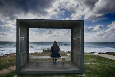 Rear view of woman sitting on bench in cabin at beach