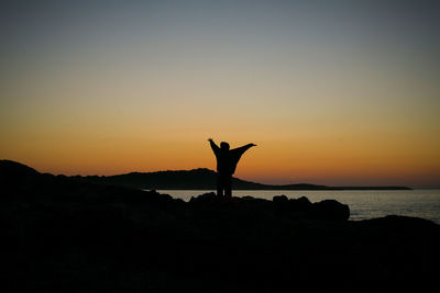 Silhouette woman with arms raised against sea during sunset