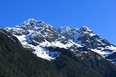 Low angle view of snowcapped mountains against clear blue sky