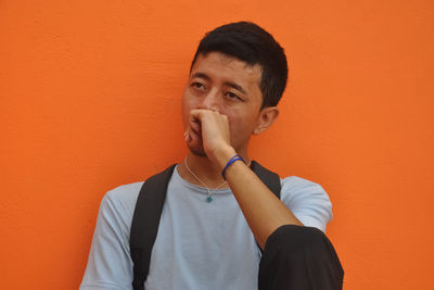 A asian young guy looking sideways posing with fist on his face, colored background with copy space 