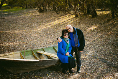 Portrait of smiling mature couple wearing sunglasses by boat at forest during autumn