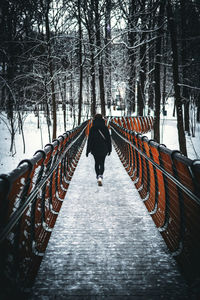 Rear view of woman walking on snow covered footbridge