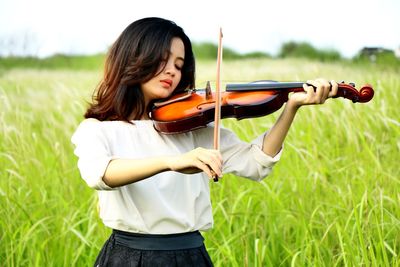 Young woman playing violin on grassy field