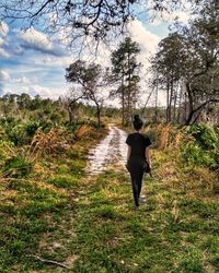 Rear view of woman walking on grass against sky