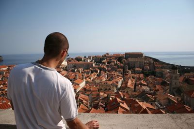 Rear view of man standing by townscape at sea shore against clear sky