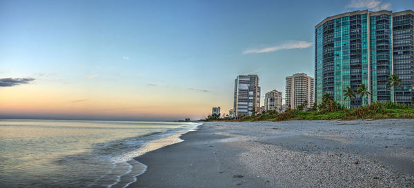 Sea and buildings against sky during sunset