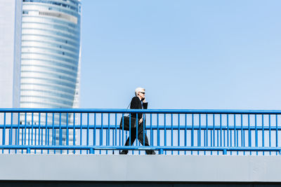 Low angle view of businessman talking over smart phone while walking on footbridge