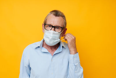 Portrait of senior man wearing mask against yellow background