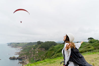 Woman with arms outstretched standing against sky