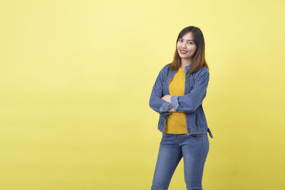 Portrait of smiling young woman against yellow background