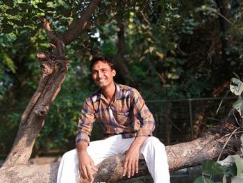 Portrait of smiling young woman sitting on tree trunk