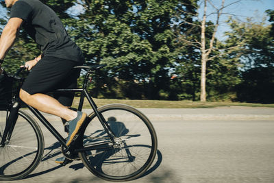 Low section of sportsman cycling on road during sunny day