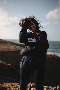Smiling young woman standing on cliff  against ocean and sky