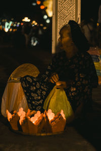 Midsection of woman sitting by illuminated lanterns at night