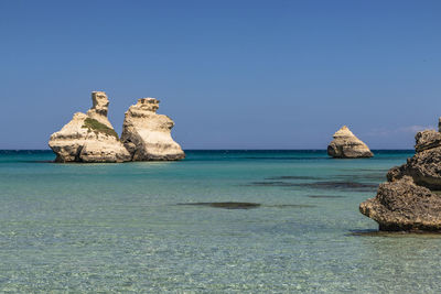 View of rock formation in sea against clear blue sky