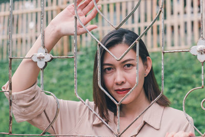 Portrait of young woman holding camera while standing by fence