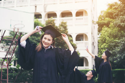 Cheerful student in graduation gown standing outdoors