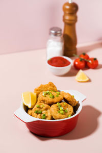 Crispy nuggets in a plate and ketchup on a pink background with hard shadows.