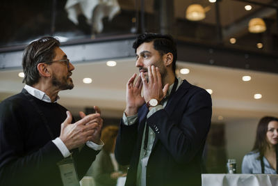 Businessmen gesturing while talking with each other during seminar