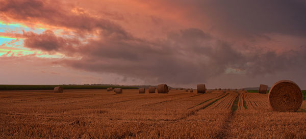 Hay bales on field against sky during sunset