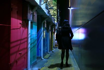 Full length rear view of woman walking on footpath amidst buildings at night