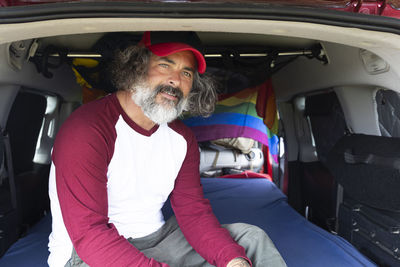 Close-up of a handsome man in a cap smiling sitting inside a camping van,